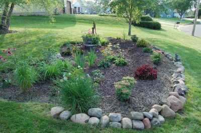 A rain garden with flowers and plants and a rock perimeter